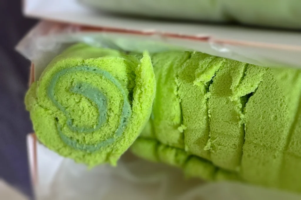 Close-up side-angle shot of homemade kaya Swiss roll made with fresh coconut and pure pandan extract, featuring a soft green sponge with kaya cream filling, freshly prepared for a fragrant Asian dessert experience.