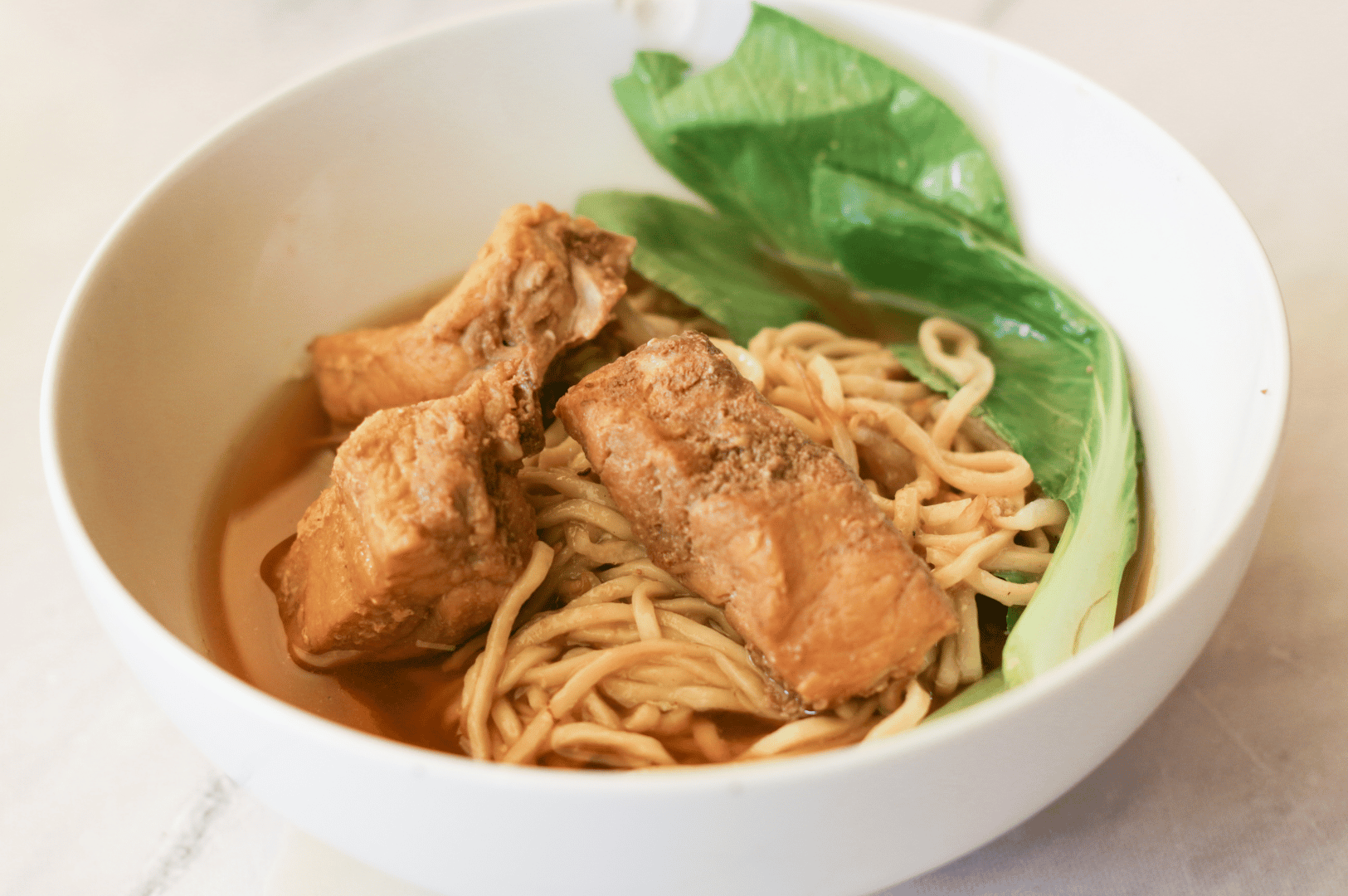 Bowl of Asian noodle soup with braised tofu and bok choy in clear broth—spotlighting a nourishing, plant-forward option for night owls dining in Singapore Chinatown after dark.