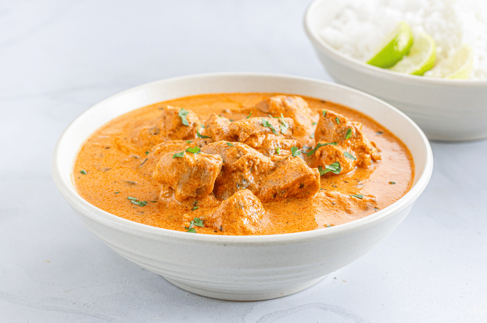 Butter chicken in creamy tomato curry garnished with cilantro, served alongside lime-topped rice—an iconic North Indian dish featured in Little India’s spice-rich dining scene.