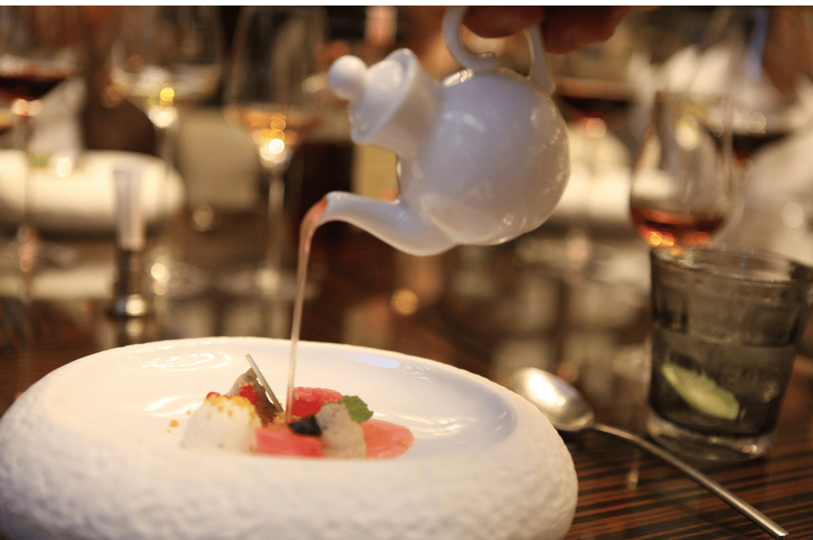 Close-up of a Michelin-level dish in Singapore with sauce being poured from a teapot over artfully plated seafood and vegetables in a refined fine dining setting.