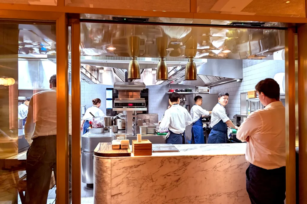 A behind-the-scenes look at the chef's table experience in a top Singapore fine dining restaurant, showing chefs actively cooking in a professional kitchen.