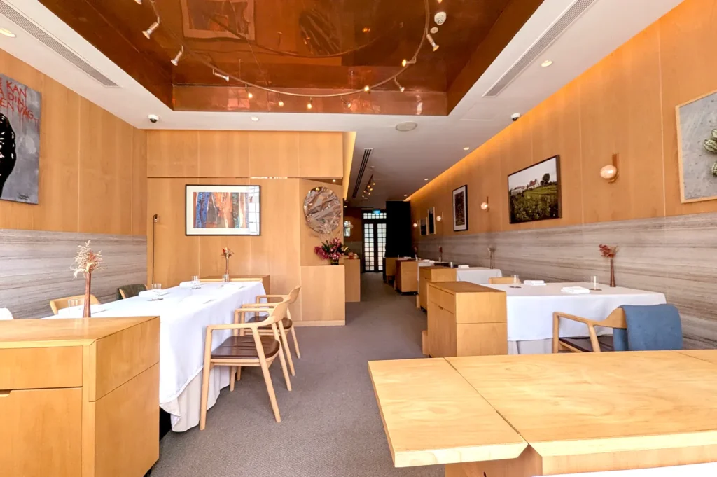 The luxurious and intimate interior of Zén Omakase in Singapore, featuring warm wooden paneling, minimalist table settings, and sophisticated art pieces.