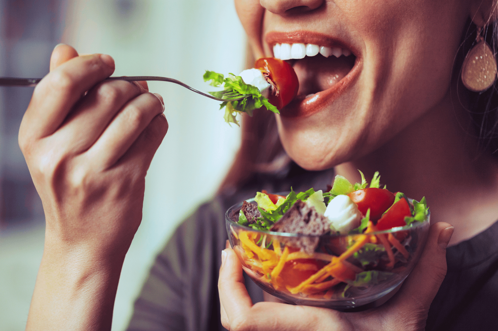 Close-up of a diner enjoying a vibrant vegan salad in Singapore, featuring cherry tomatoes, shredded carrots, leafy greens, and plant-based dressing in a glass bowl.