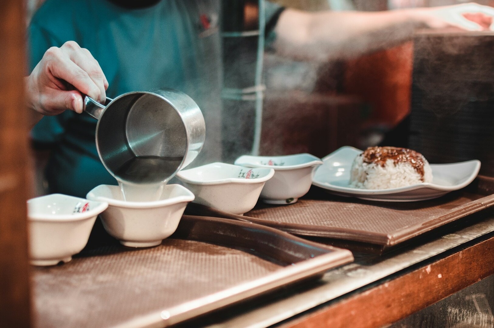 A person carefully pours hot water into a bowl, showcasing culinary techniques in action.