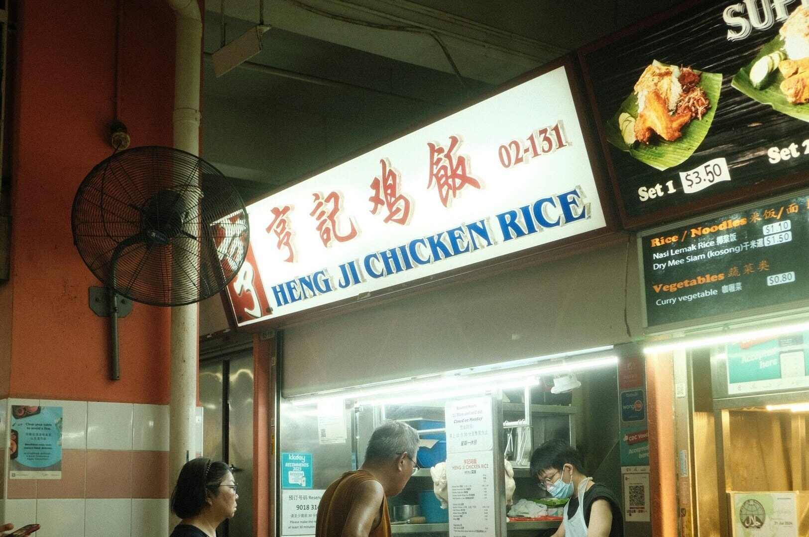 A couple poses in front of Hainanese Chicken Rice Hawker Stall, showcasing the restaurant's vibrant atmosphere.