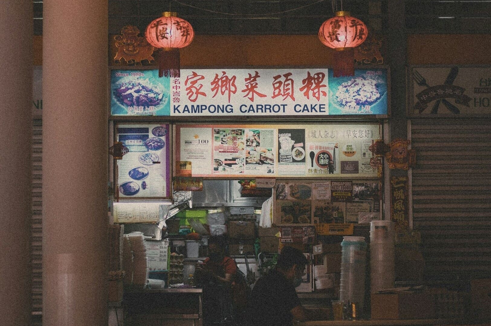 A man sitting at a table outside a Chinese restaurant, with a carrot cake in front of him.