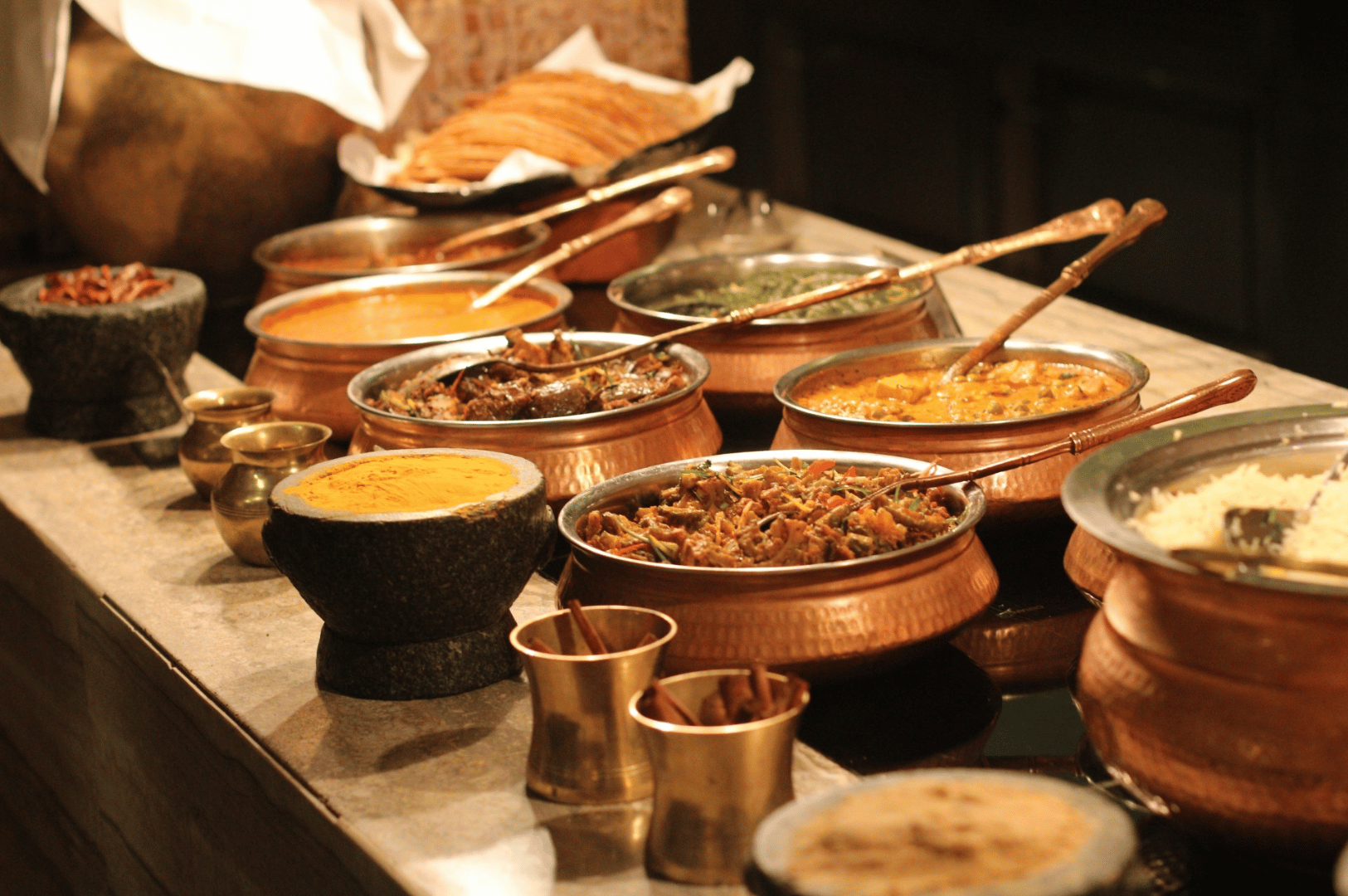 Buffet spread of Indian curries, rice, and flatbreads in traditional serving ware, reflecting the communal richness and spice-forward variety of Little India’s restaurant scene.