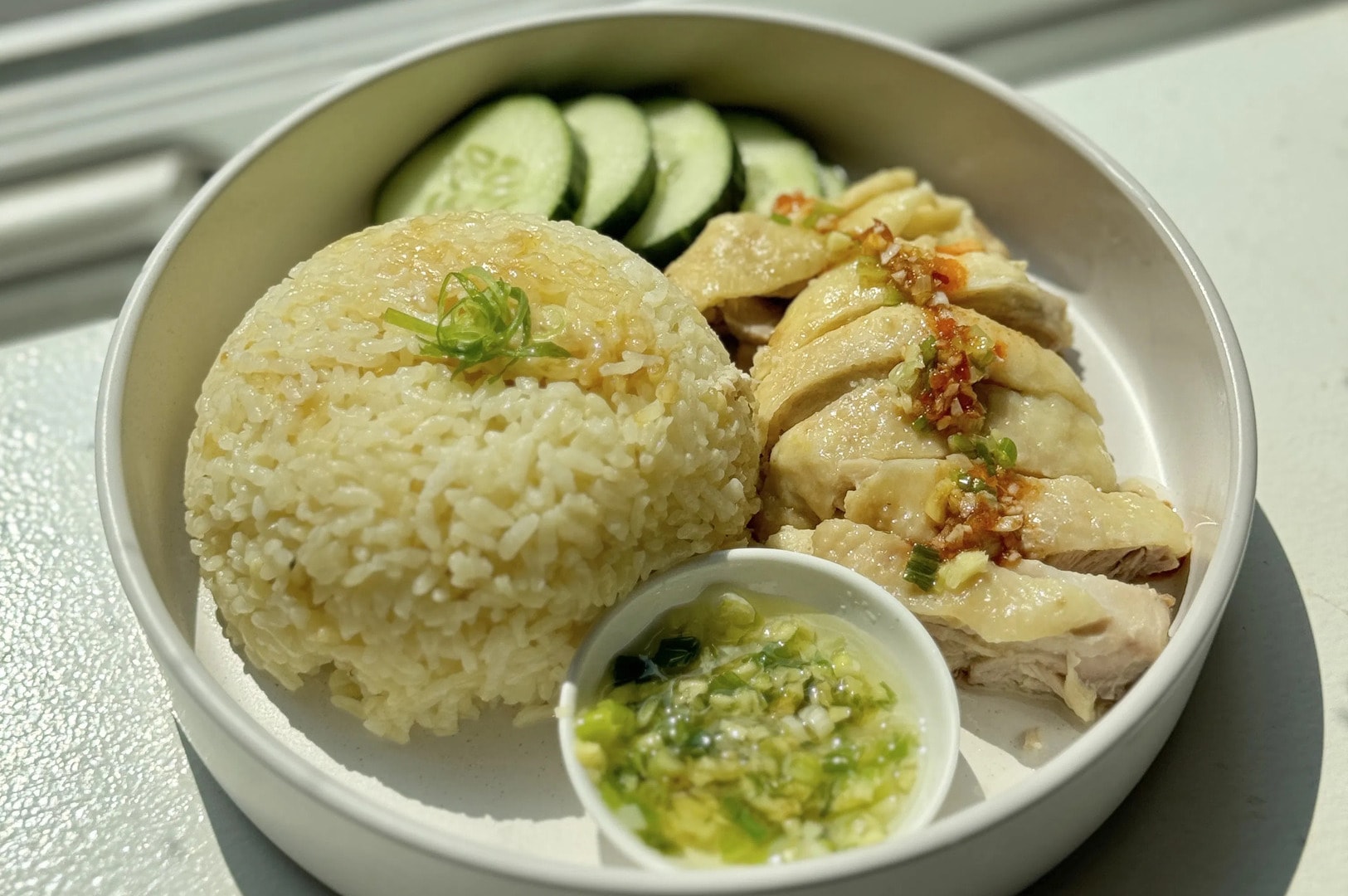 Hainanese chicken rice served on a plate, showcasing succulent chicken, aromatic rice, and crisp cucumber.