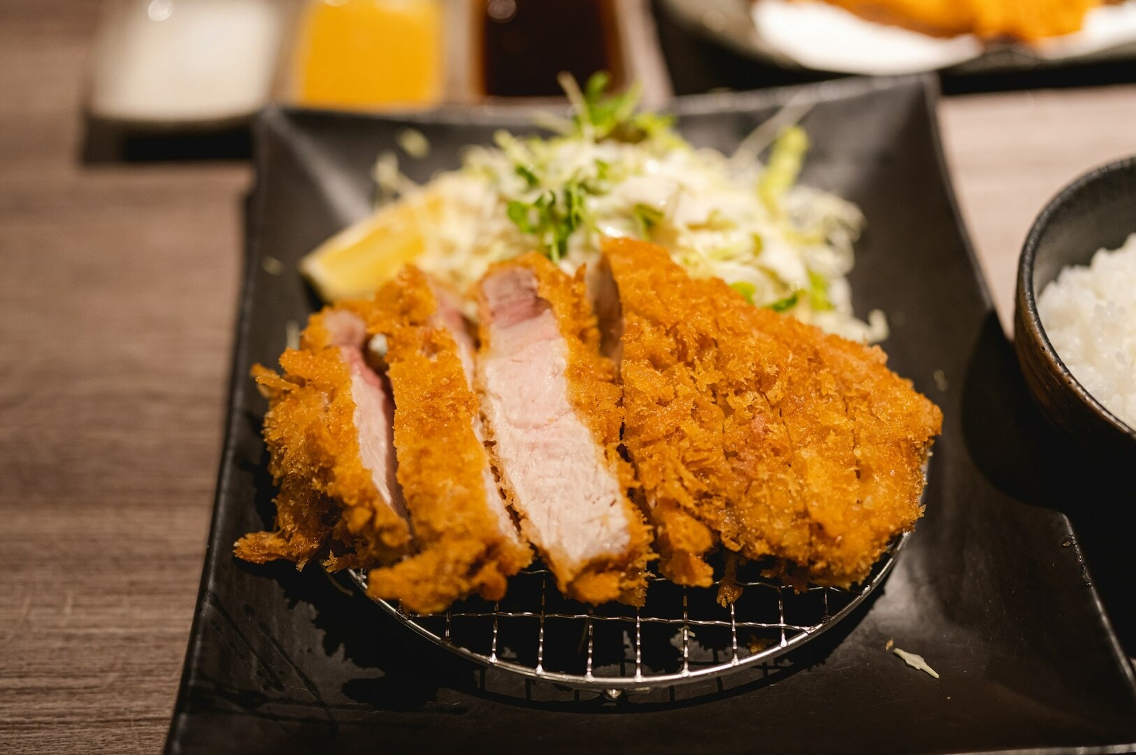 Close-up of crispy, golden-brown fried pork cutlets on a black plate, served with shredded cabbage and lemon wedge, evoking a savory and appetizing tone.