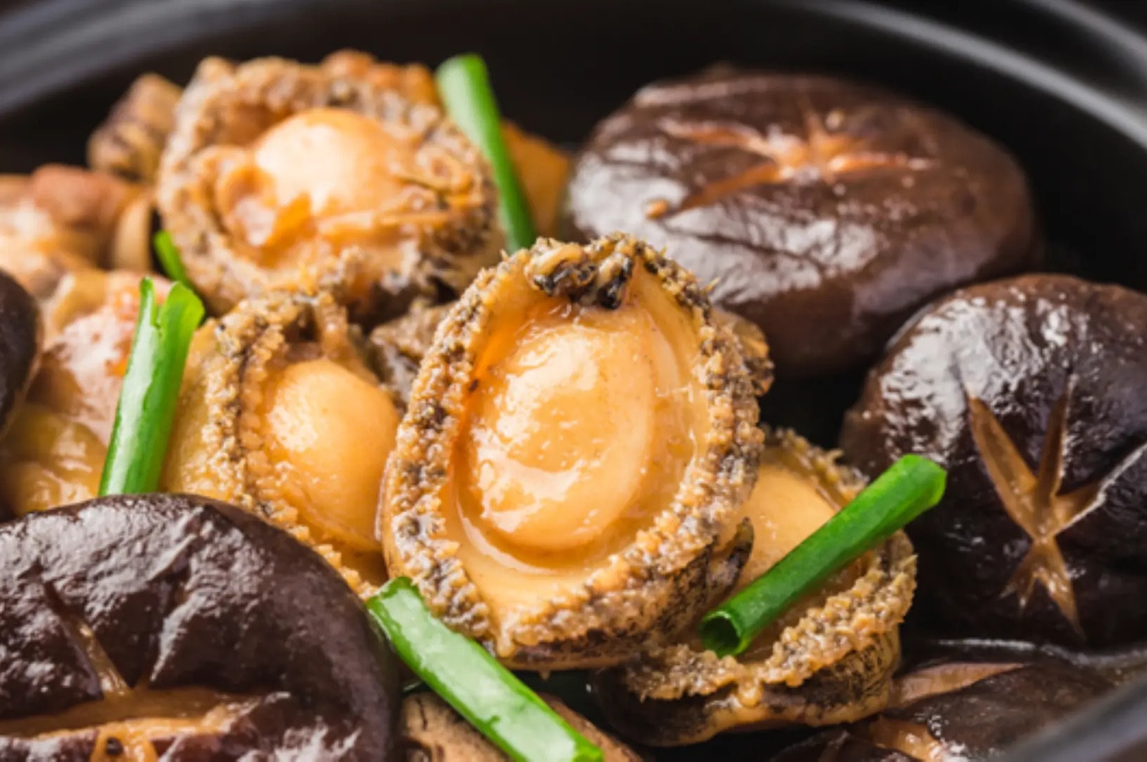 A bowl of braised abalone featuring cooked mushrooms and green onions, symbolizing prosperity for Chinese New Year.