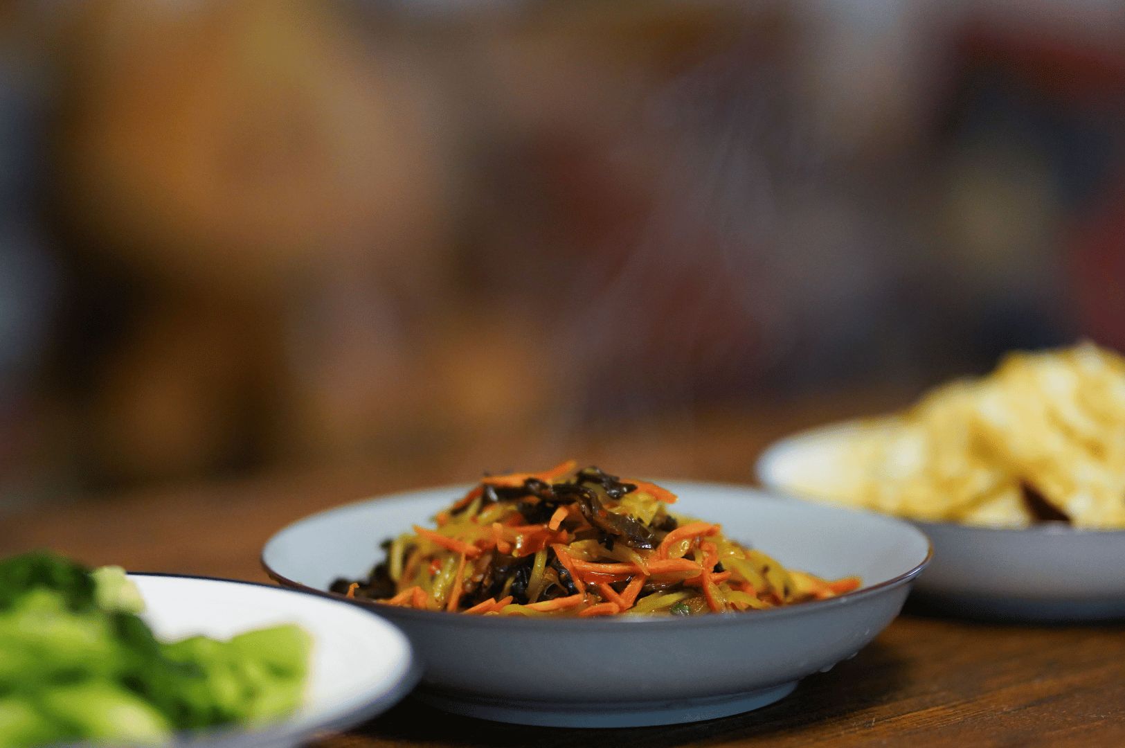 Colorful vegan spread at a Singapore plant-based restaurant featuring stir-fried noodles with mushrooms and carrots, steamed broccoli, and crispy wonton chips on rustic wood.