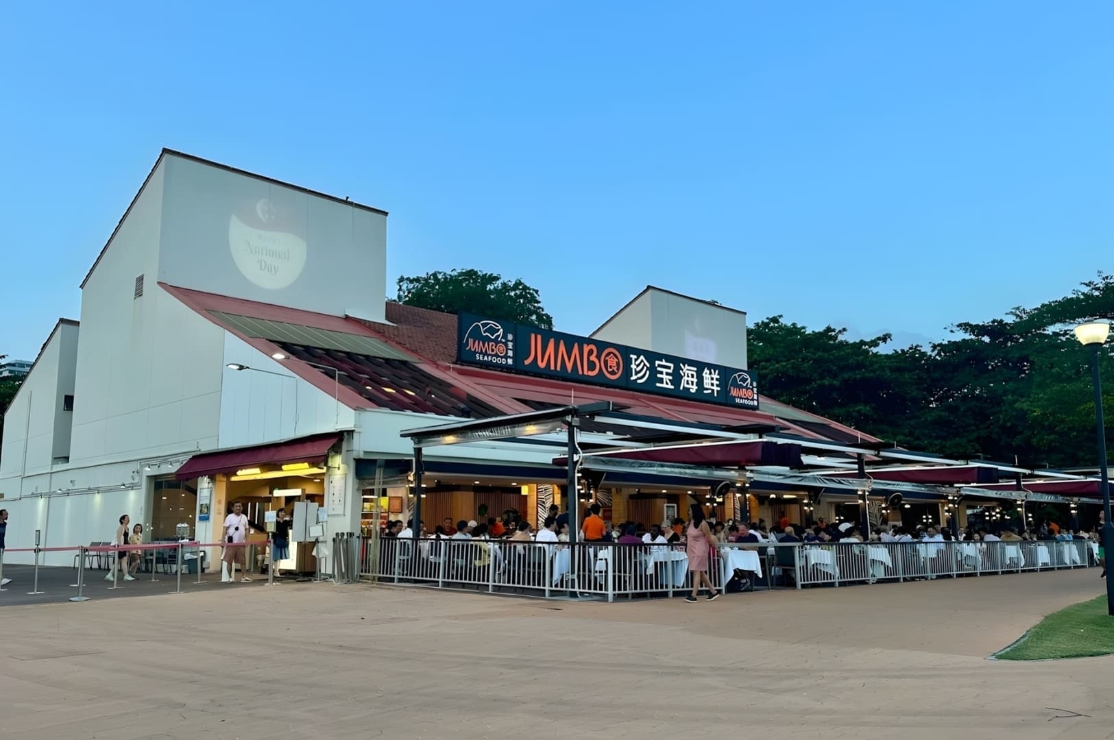 Outdoor dining at Jumbo Seafood in East Coast Park, Singapore, with patrons enjoying meals and a prominent restaurant sign.