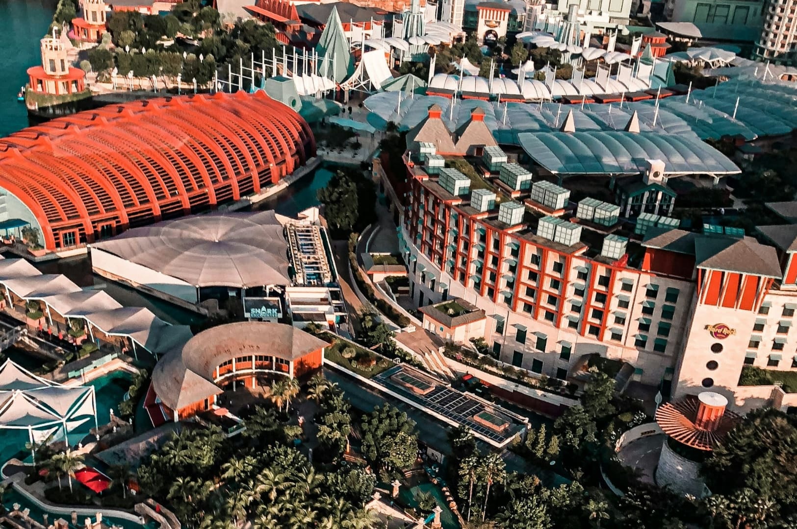 Aerial view of a vibrant resort complex with colorful, modern architecture, lush greenery, and a tranquil waterfront, exuding a lively, tropical atmosphere.