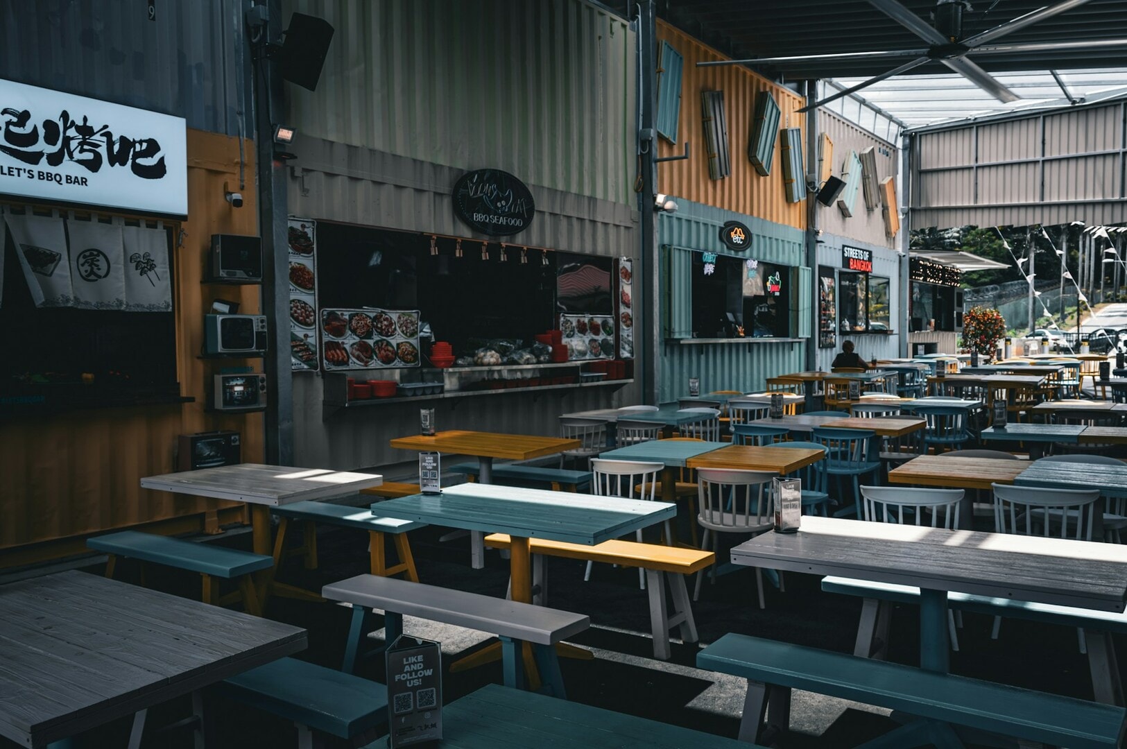 A bustling Singapore Hawker restaurant featuring tables and chairs arranged in the center of the building.