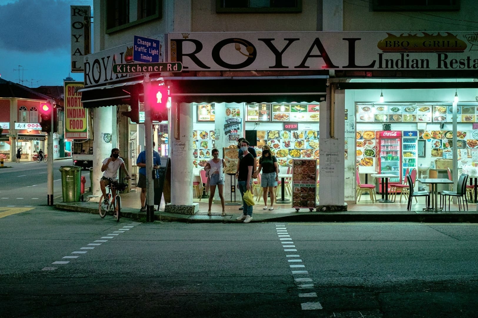 A street scene featuring a Singapore restaurant with outdoor seating and vibrant signage.