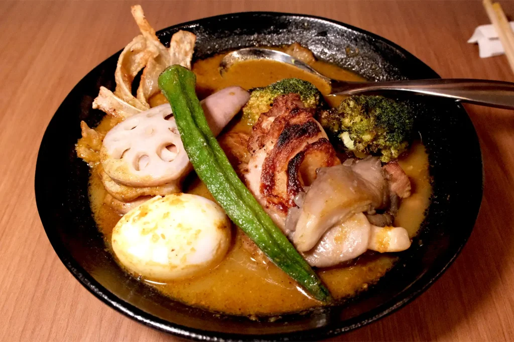 A rich and fragrant bowl of signature chicken soup curry from Soup Curry by Ki-setsu at Fortune Centre, generously loaded with toppings such as charred broccoli, lotus root chips, okra, a soft-boiled egg, and tender chicken.
