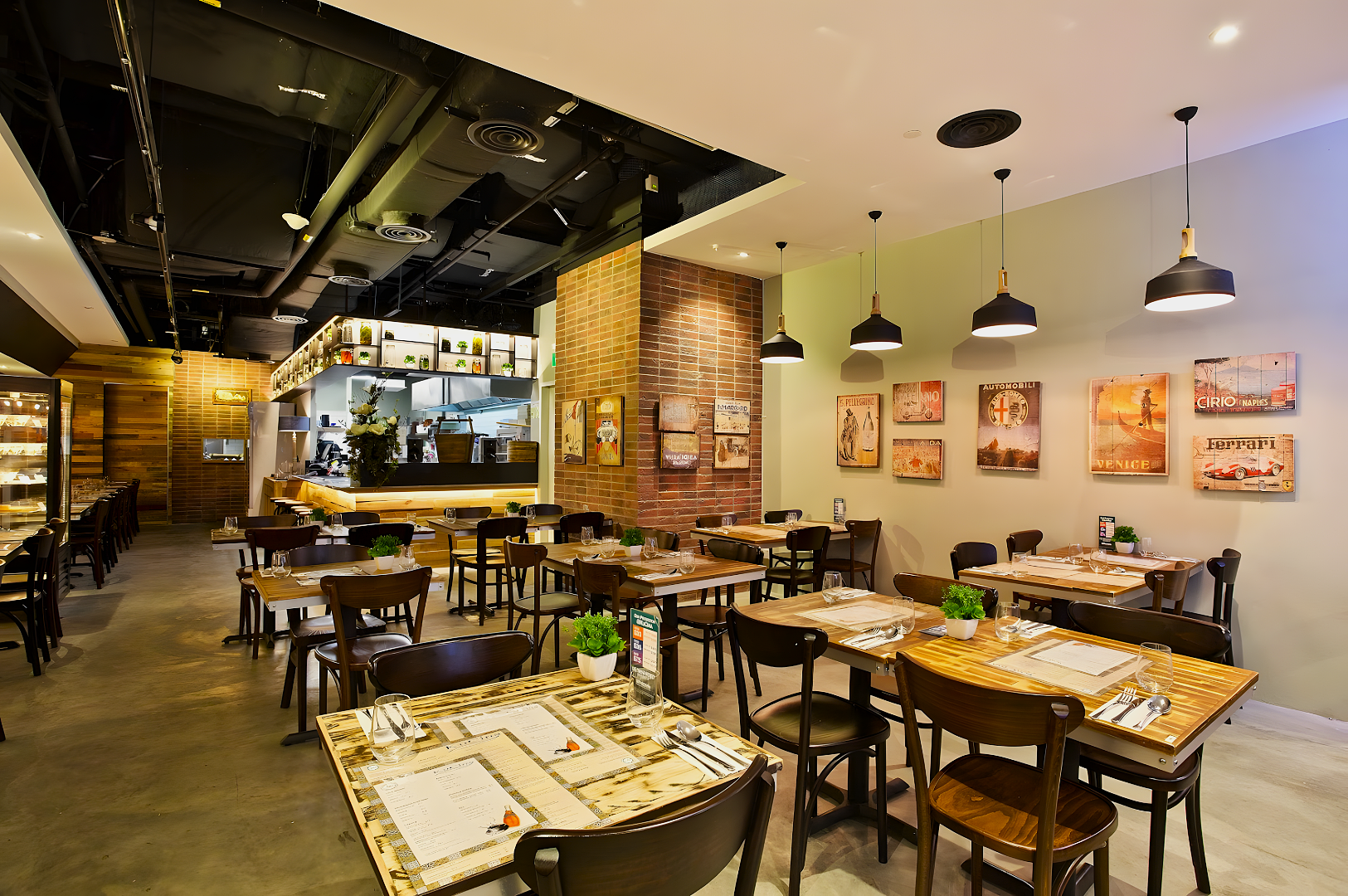 Spacious, modern restaurant with wooden tables set for dining. Brick accent wall, vintage posters, pendant lights create a warm, inviting atmosphere.