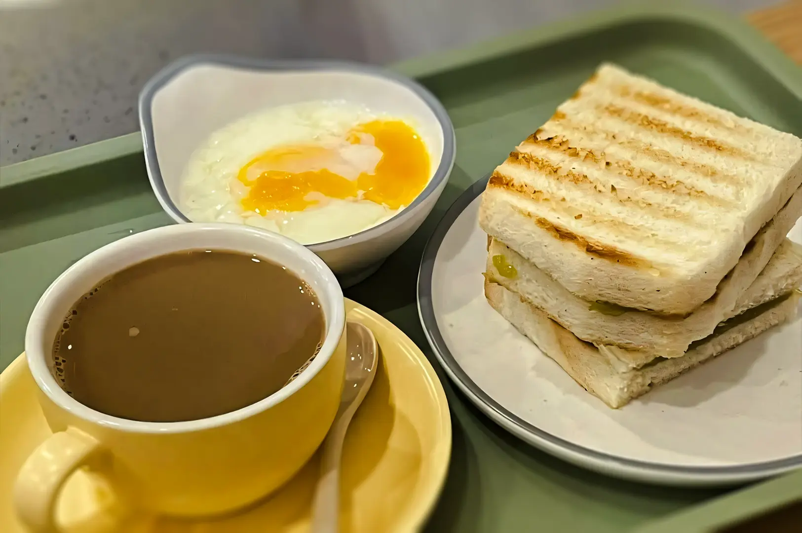 Classic Singapore breakfast set with kaya toast, soft-boiled eggs drizzled with soy sauce, and a cup of hot coffee served on a tray.