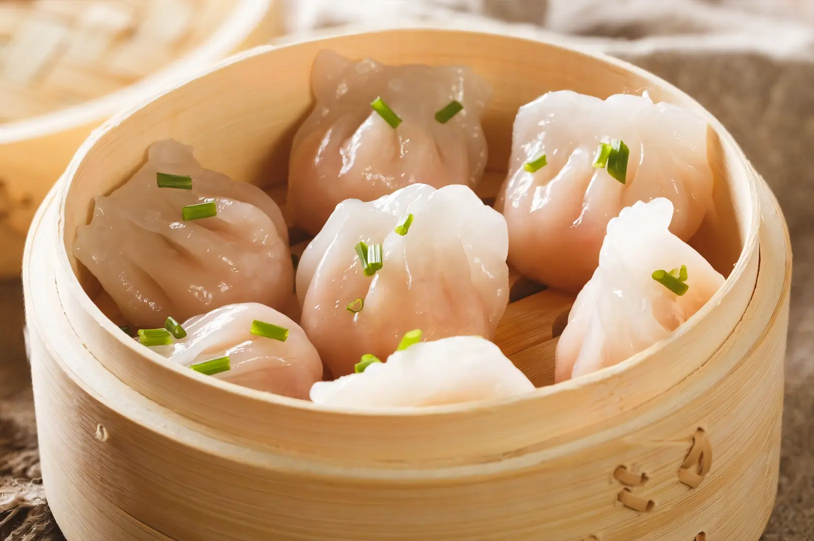 Steamed har gow shrimp dim sum served in a bamboo dim sum basket, topped with fresh chives.