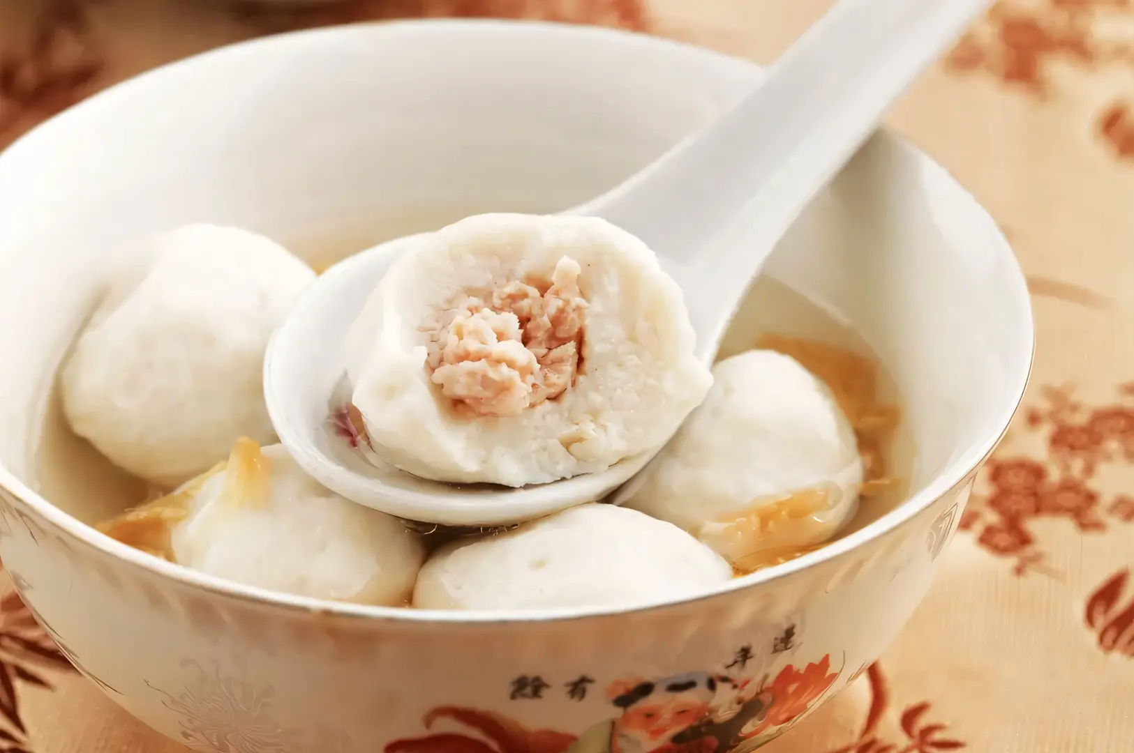 Bowl of fish ball soup with a spoon lifting a stuffed fish ball, served in a clear savory broth.