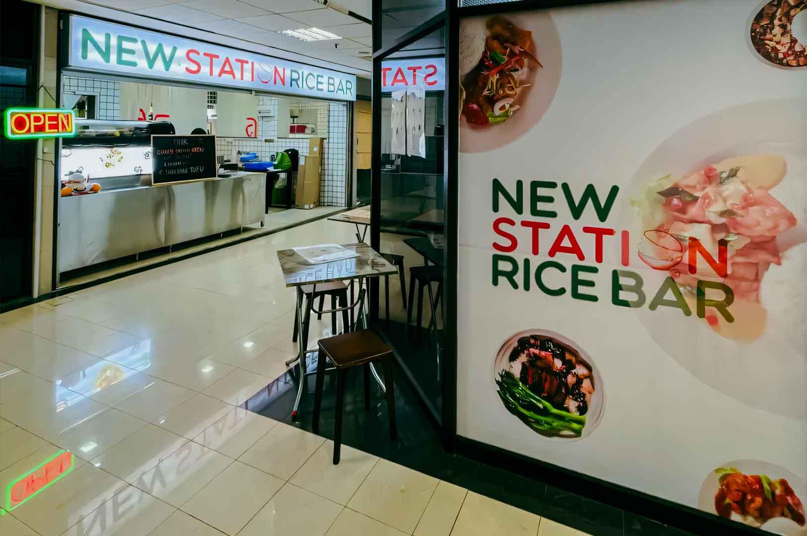 New Station Rice Bar with illuminated signage, counter service area, and small dining tables near the entrance.