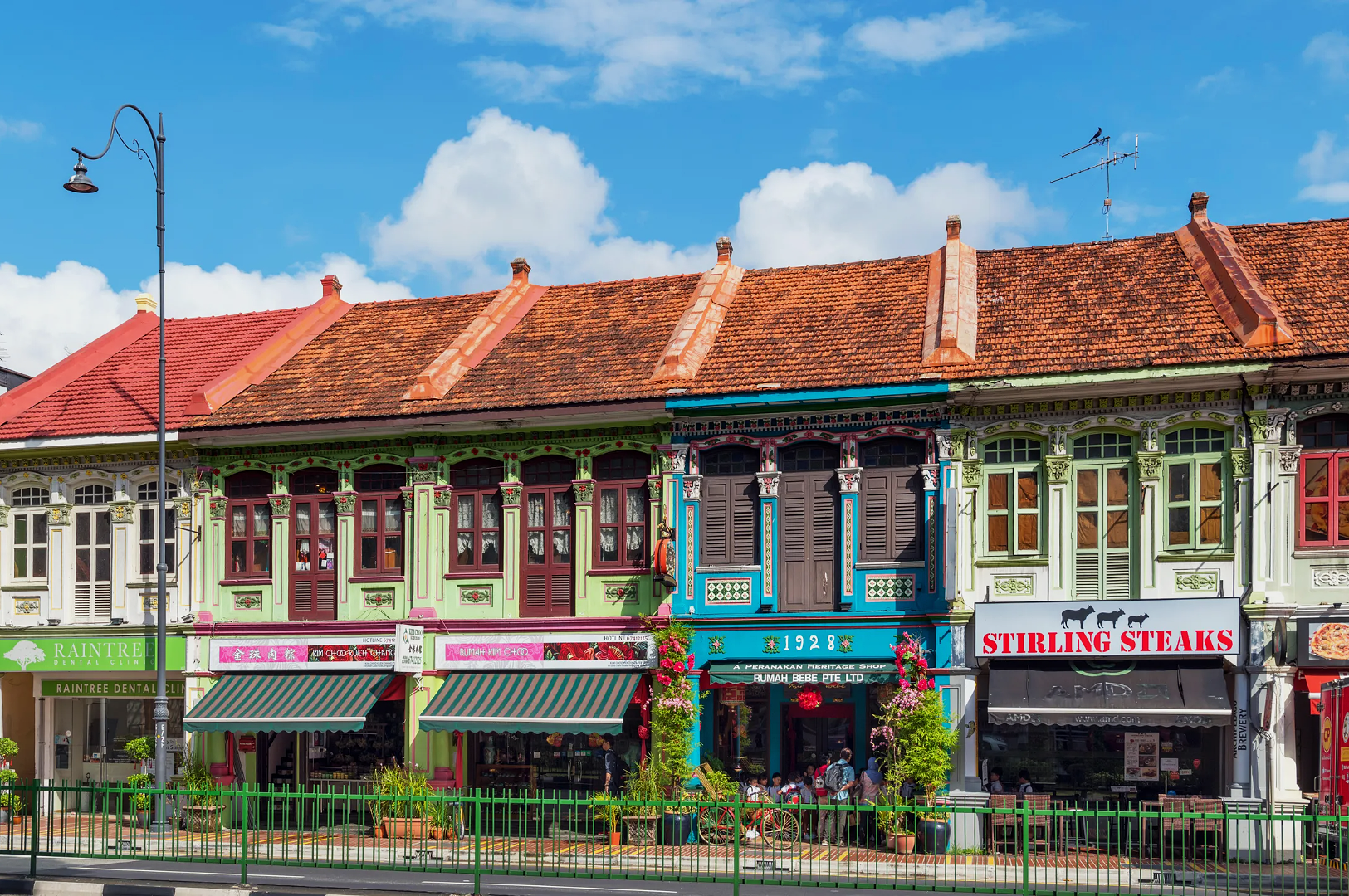 Colorful row of historic shophouses with ornate details in bright sunlight, featuring vibrant store signs and a clear blue sky above.