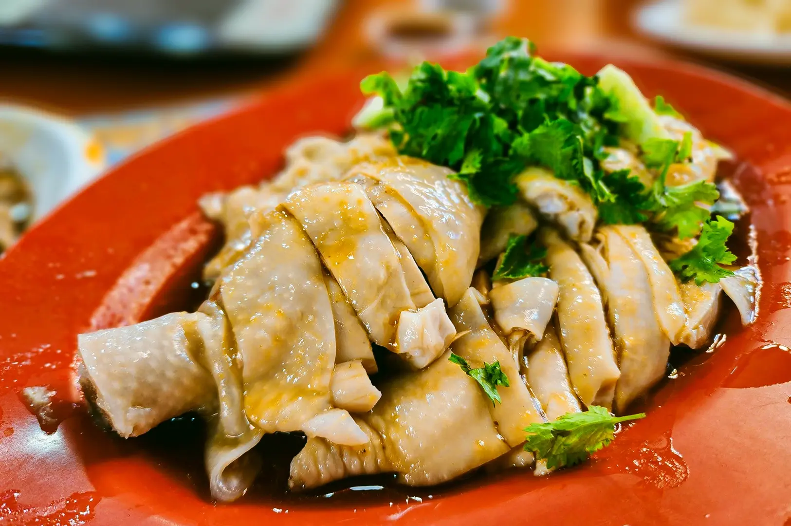 Plate of Hainanese chicken rice with tender poached chicken slices topped with fresh cilantro and served in a light soy and sesame dressing.