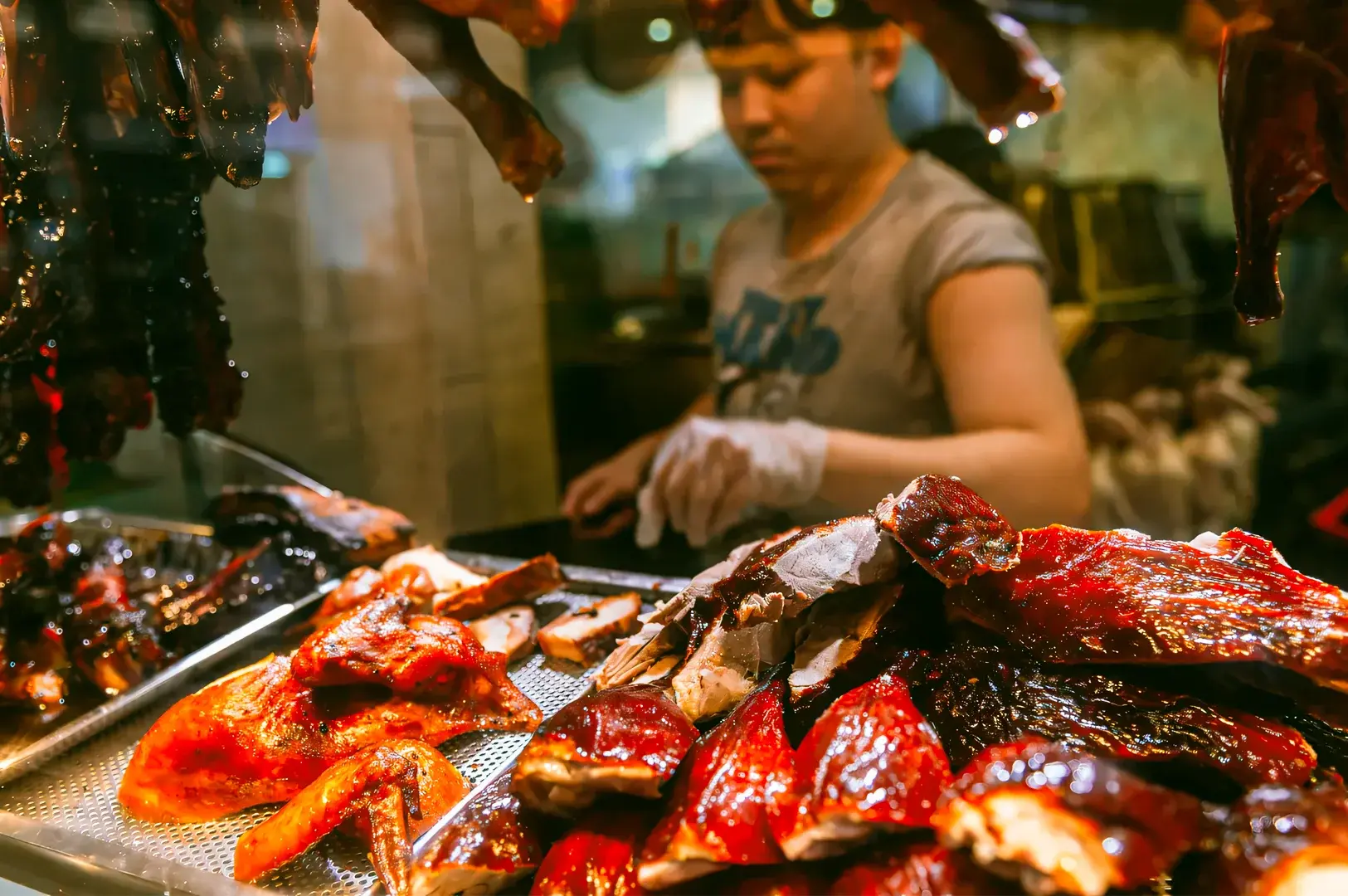 Display of glistening roasted meats including char siew, roast duck, and crispy pork arranged on a metal tray at a Singapore hawker stall.