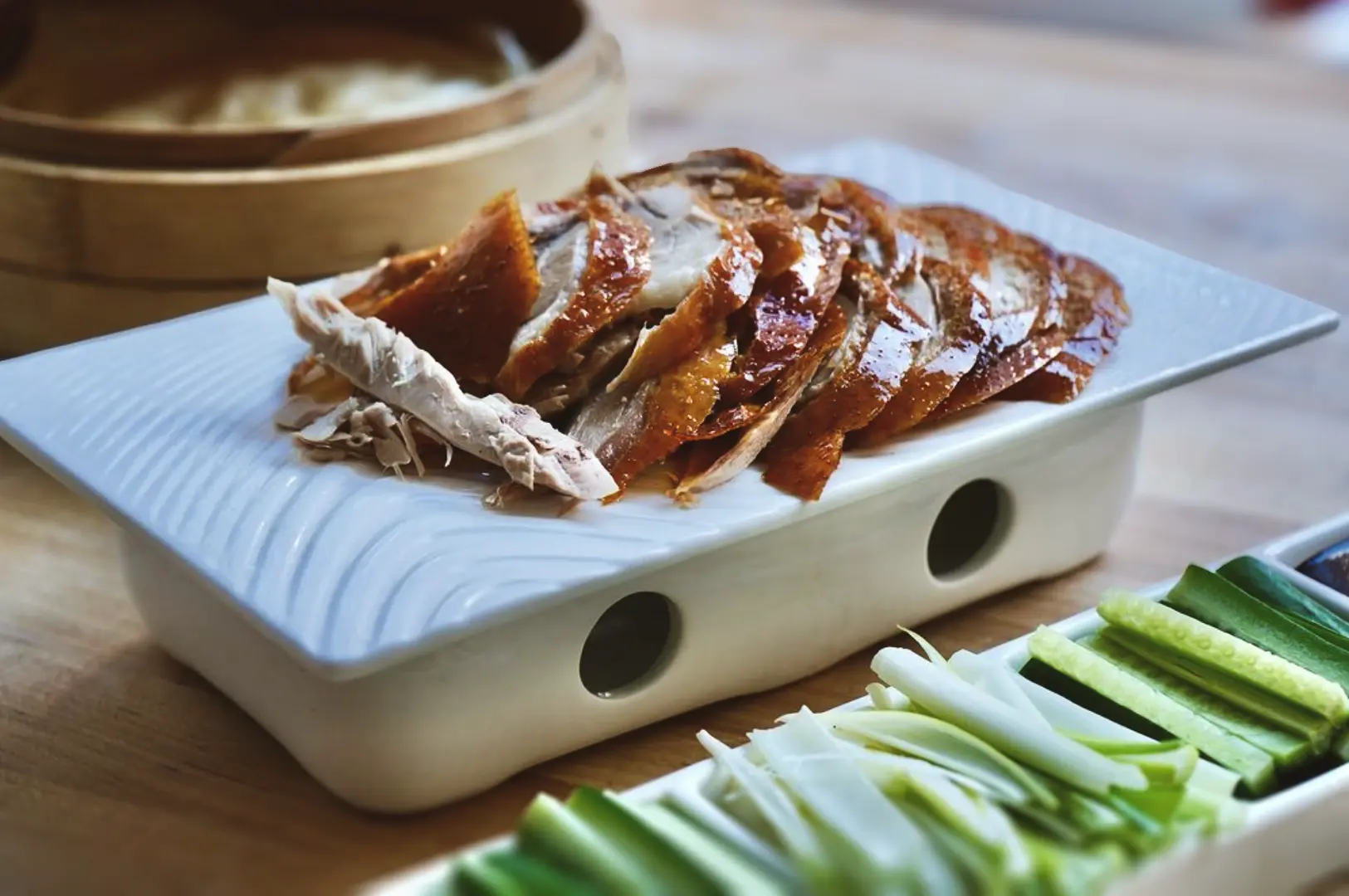 Platter of sliced roast duck with crispy skin served alongside julienned vegetables and traditional wrappers.