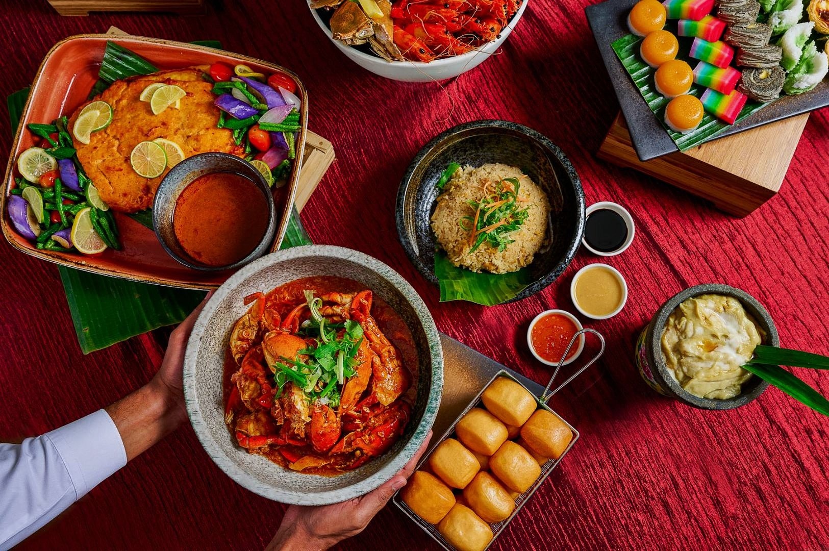 A vibrant spread of diverse Asian dishes on a red tablecloth. Includes crab in rich sauce, fried rice, colorful desserts, and dipping sauces, creating an inviting, festive mood.