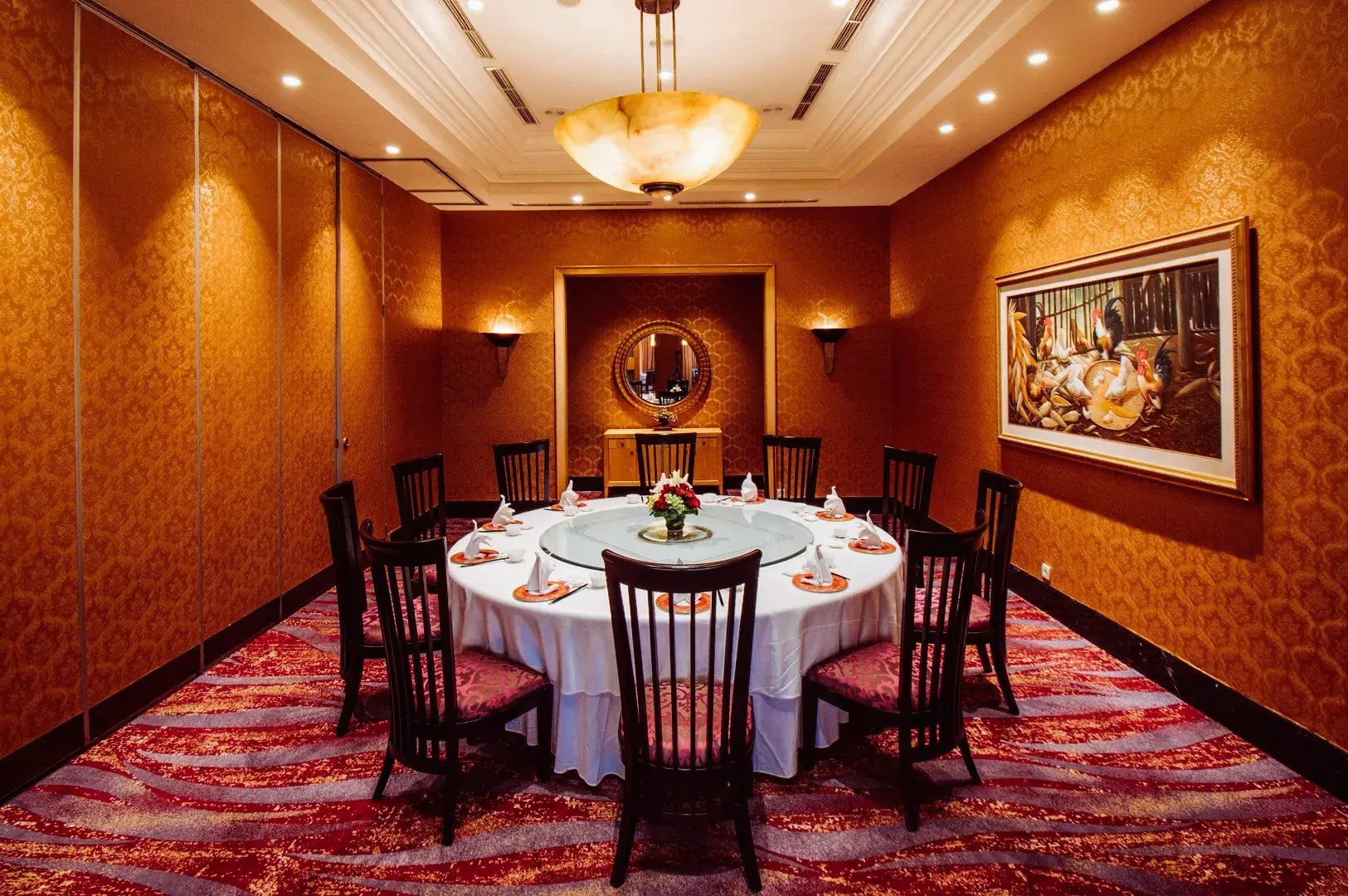 Upscale private dining room with a large round table set for guests, warm patterned walls, and soft ambient lighting.