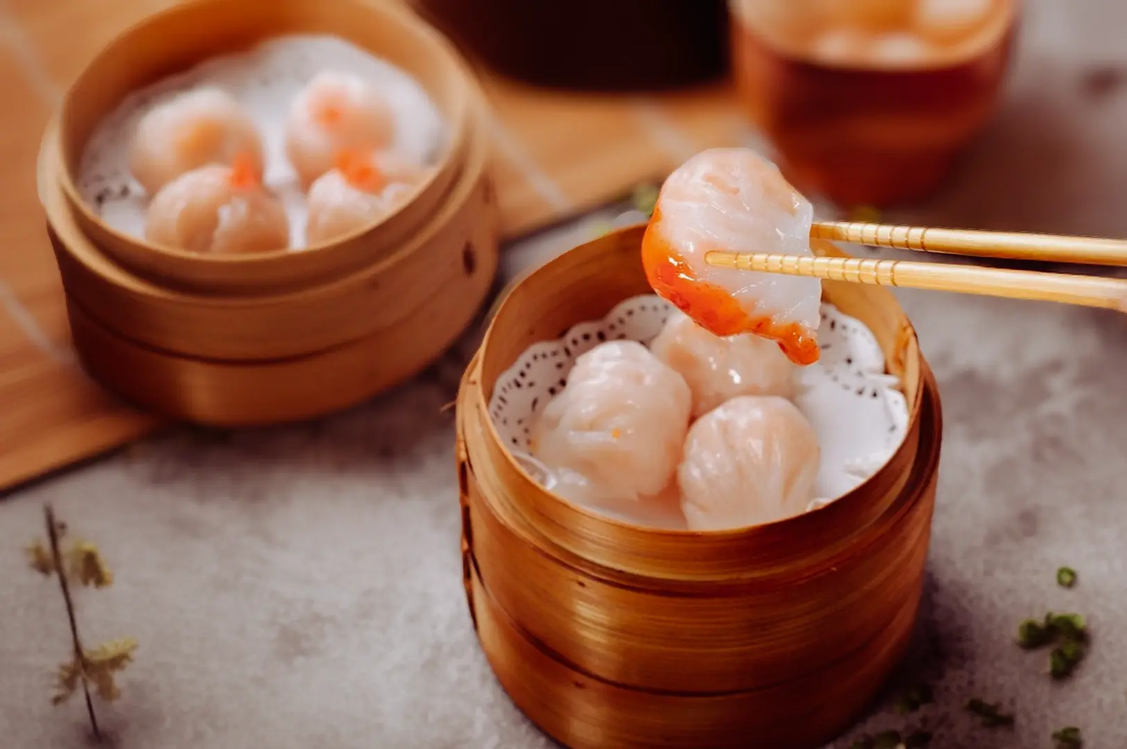 Steamed har gow shrimp dim sum in a traditional bamboo steamer, with a dumpling being lifted by chopsticks.