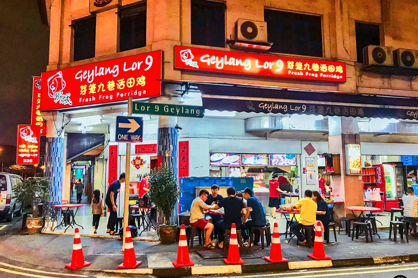 Nighttime view of Geylang Lor 9 Fresh Frog Porridge restaurant with bright red signage, outdoor seating, and illuminated storefront along Geylang Road.