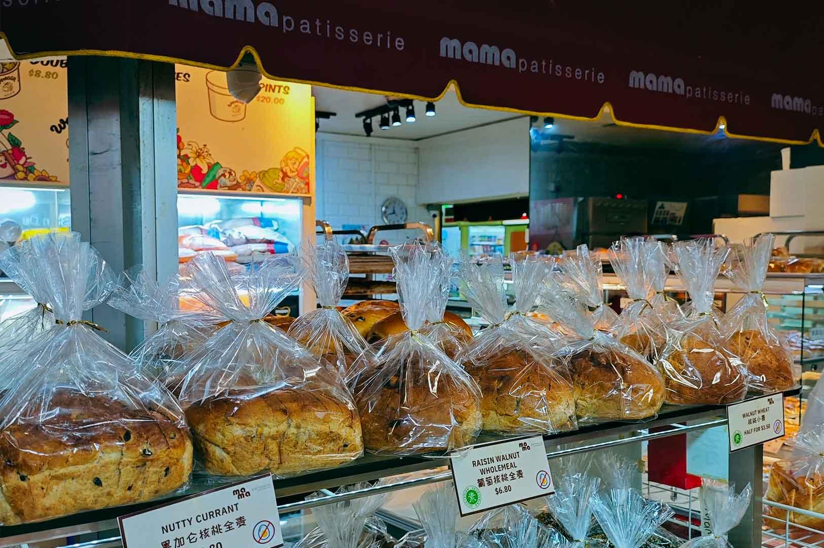 Rows of freshly packed loaves displayed on metal shelves at Mama Patisserie inside Fortune Centre, with price tags and bakery equipment visible in the background.