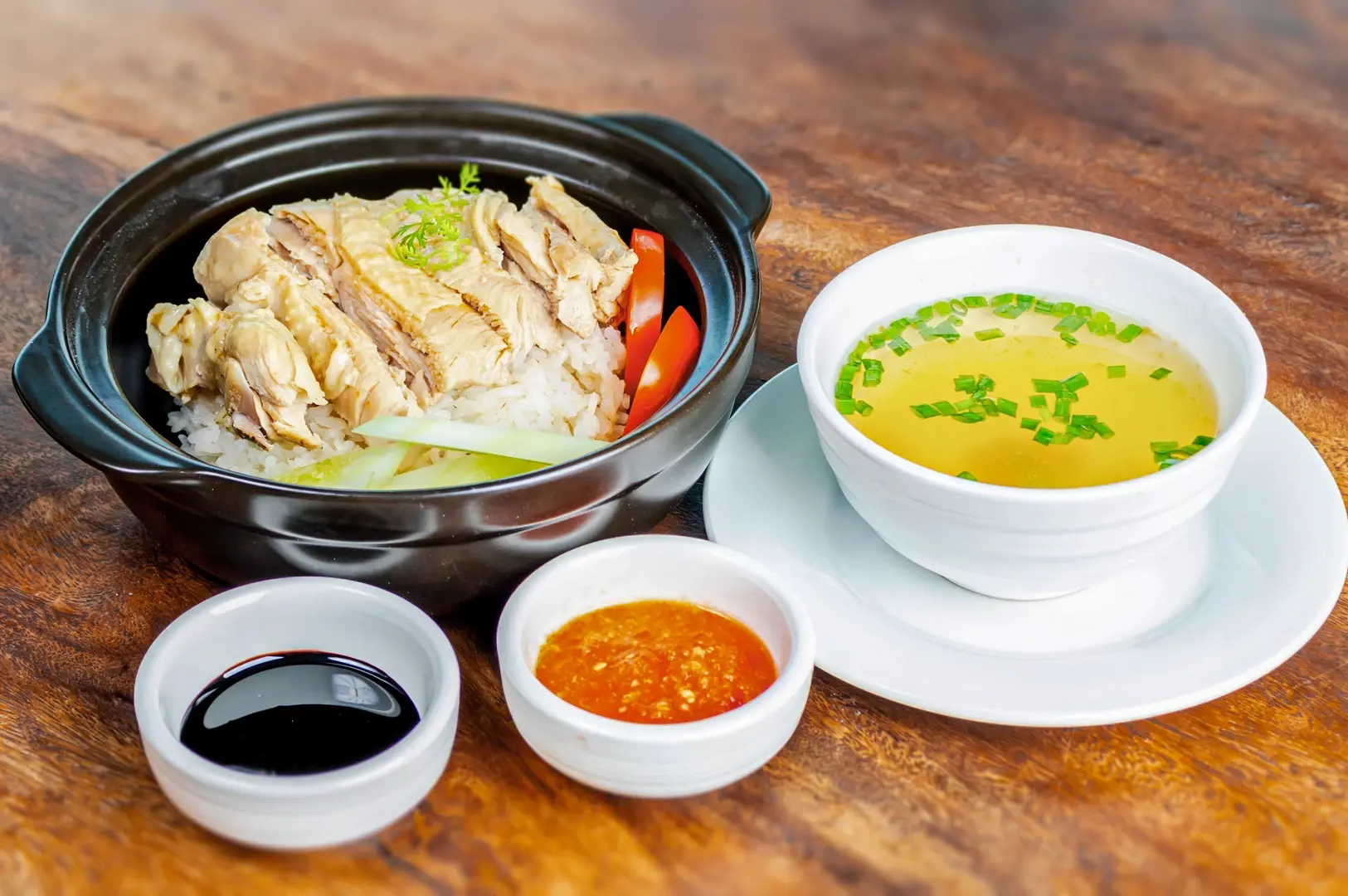  Hainanese chicken rice from Singapore served with steamed chicken, fragrant rice, chili sauce, ginger paste, and clear soup.