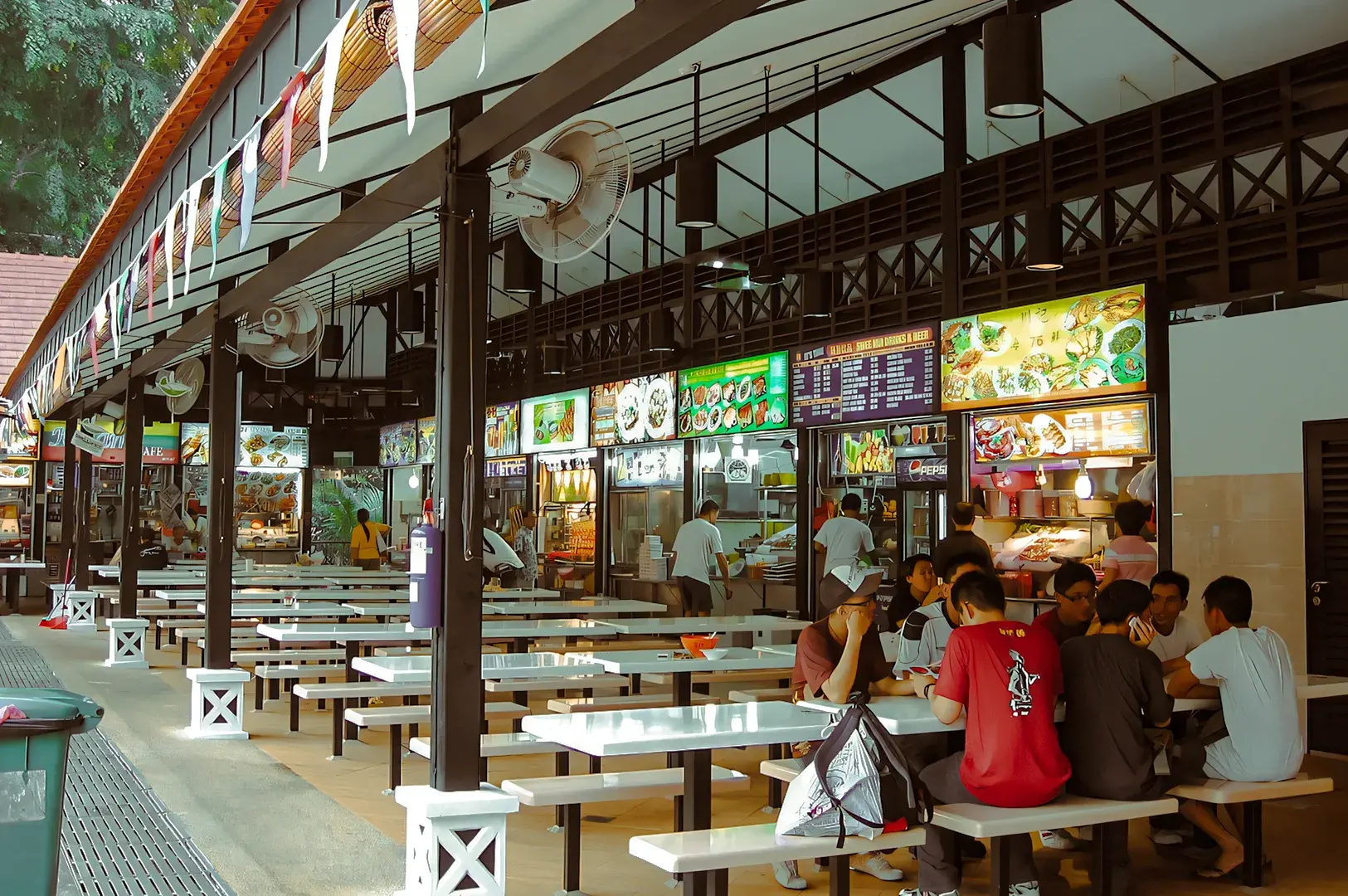 Busy Singapore hawker centre with long communal tables, local food stalls, and illuminated menu boards offering street food.