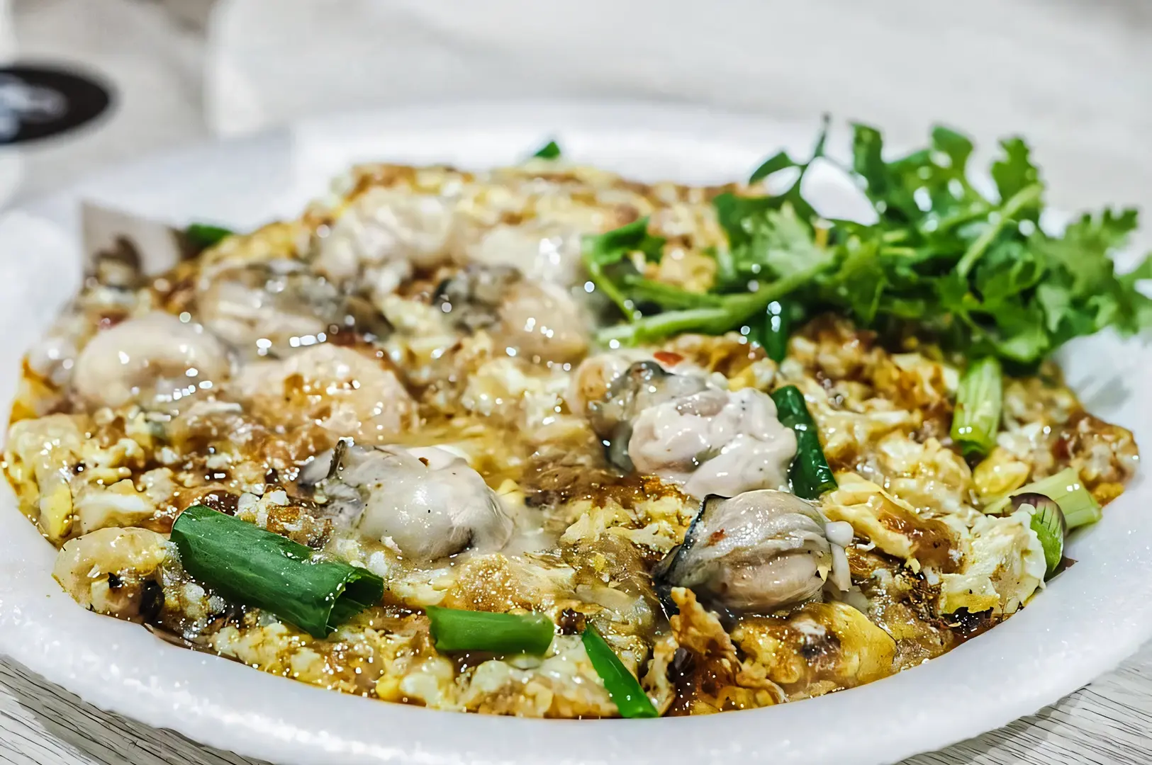 Crispy Singapore oyster omelette with fresh oysters, eggs, and spring onions, served on a white plate.
