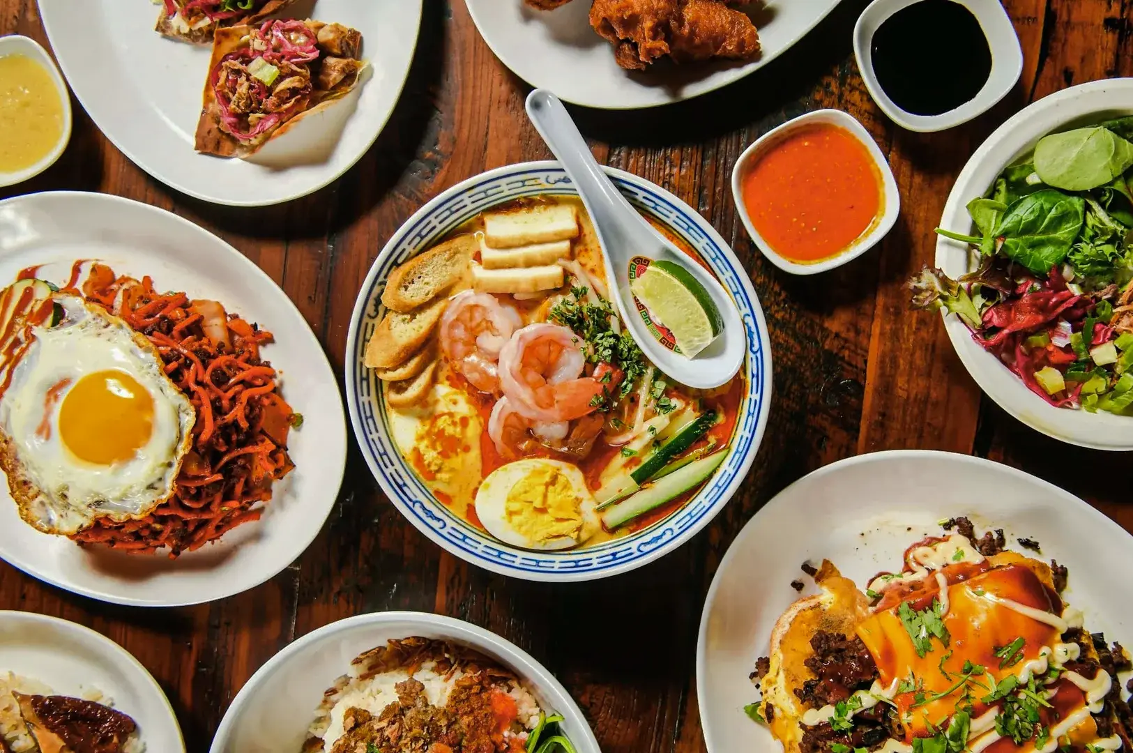 Assorted Singapore hawker dishes on a table, including laksa, char kway teow, fried egg noodles, and local side dishes.