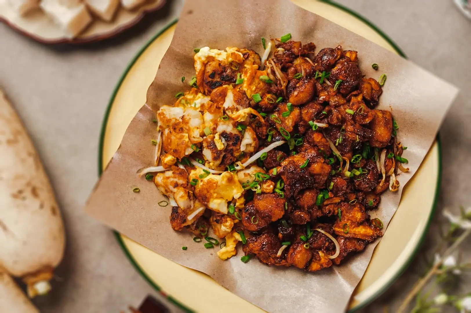 Singapore street food platter featuring fried carrot cake and savory stir‑fried dishes topped with scallions and spices.