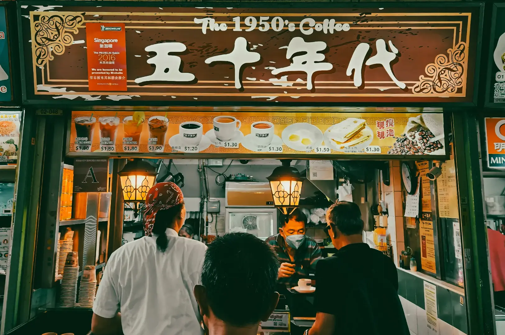 Frontal eye-level street shot of The 1950s Coffee stall with visible menu signage, illuminated counter lights, and customers standing in front of the entrance.
