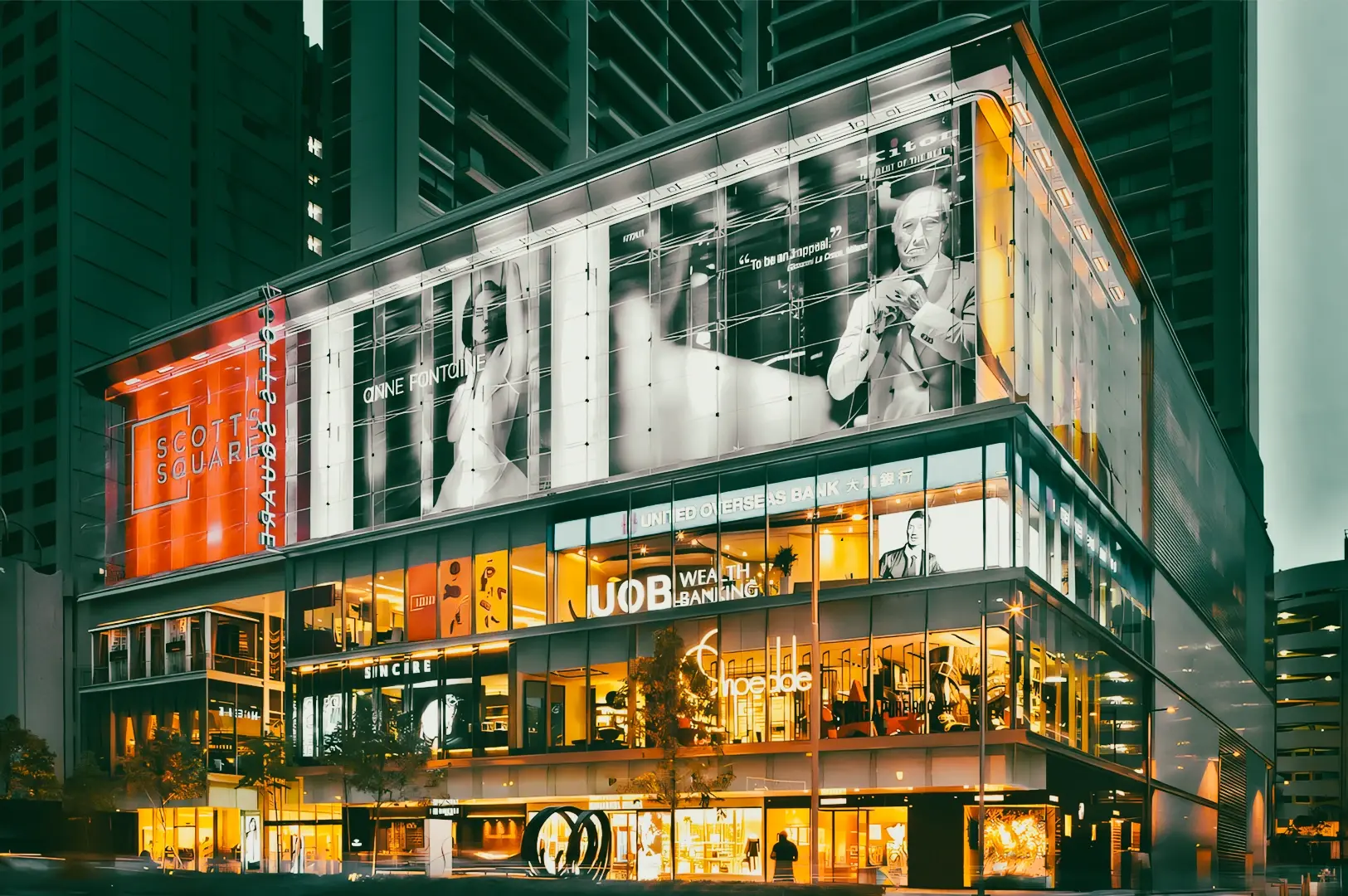Low-angle nighttime exterior shot of Scotts Square on Orchard Road with illuminated retail and dining spaces