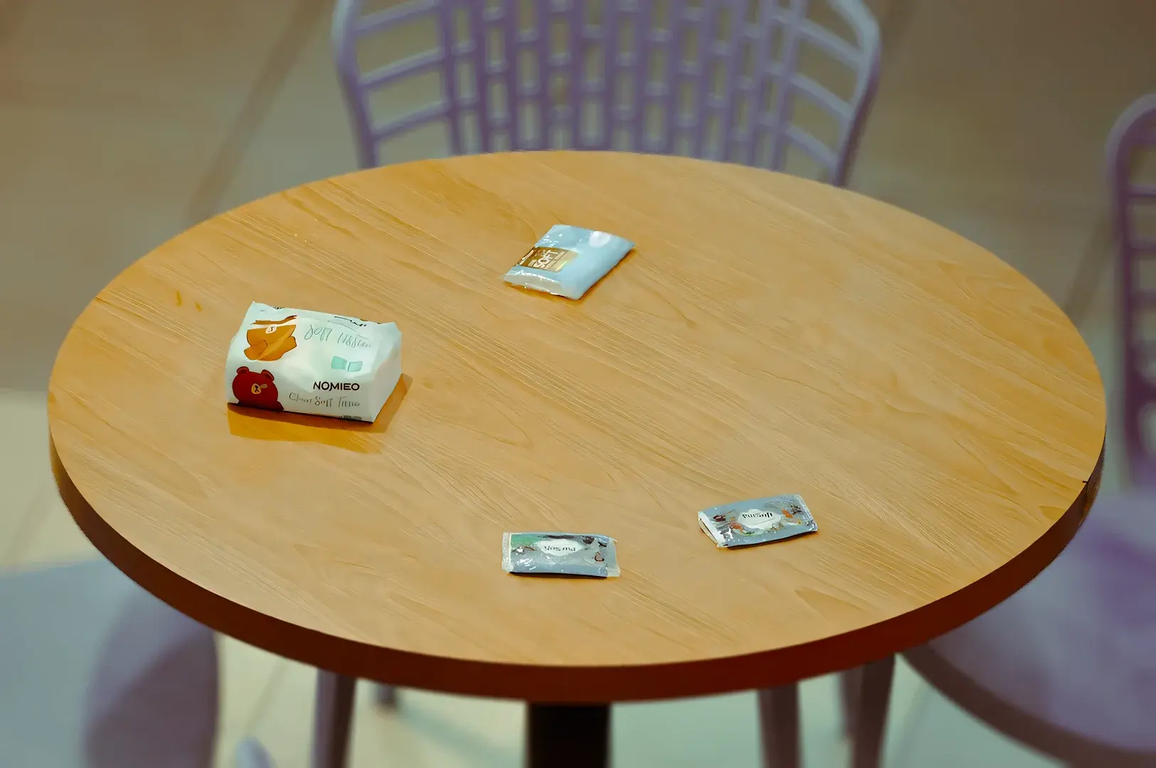 High‑angle minimalist shot of a round wooden café table with chairs and tissue packets placed on the tabletop, illustrating Singapore chope culture where tissues are used to reserve seats.