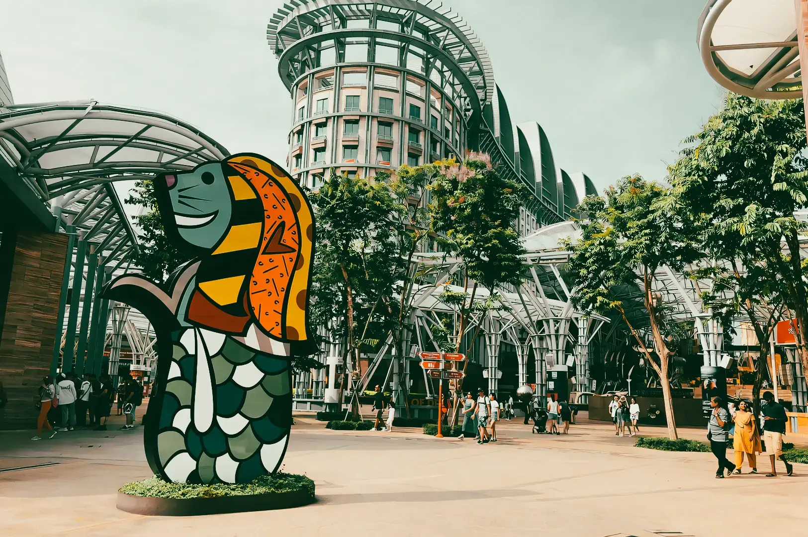 Wide-angle outdoor shot of Resorts World Sentosa Singapore featuring public art sculpture, modern resort architecture, landscaped walkways, and surrounding dining precinct