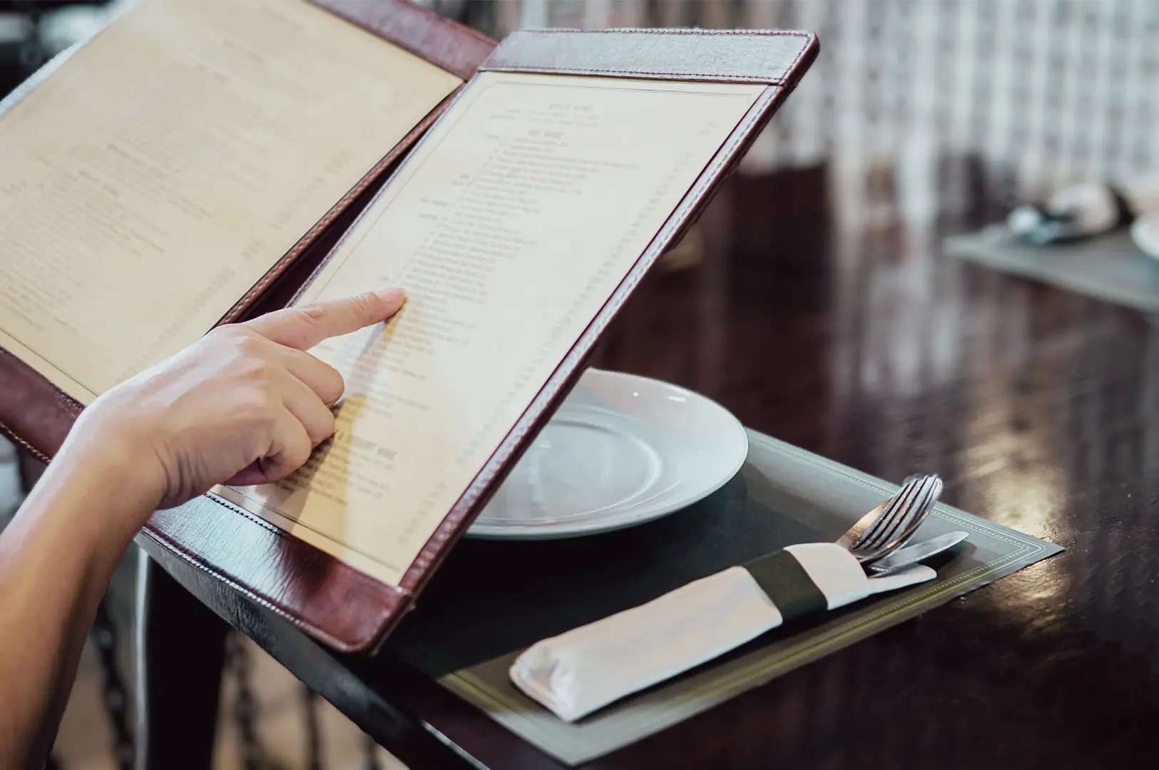 Over-the-shoulder close-up shot of a restaurant menu being reviewed at a dining table, highlighting the decision-making process when choosing dishes in a casual dining setting.