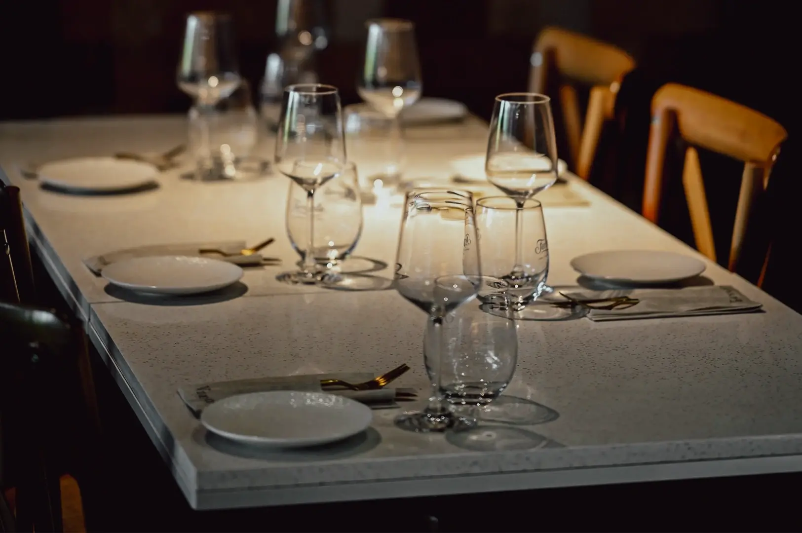 Eye-level close-up shot of an elegant restaurant table setting with wine glasses, ceramic plates, and minimalist décor, showcasing refined fine dining details.
