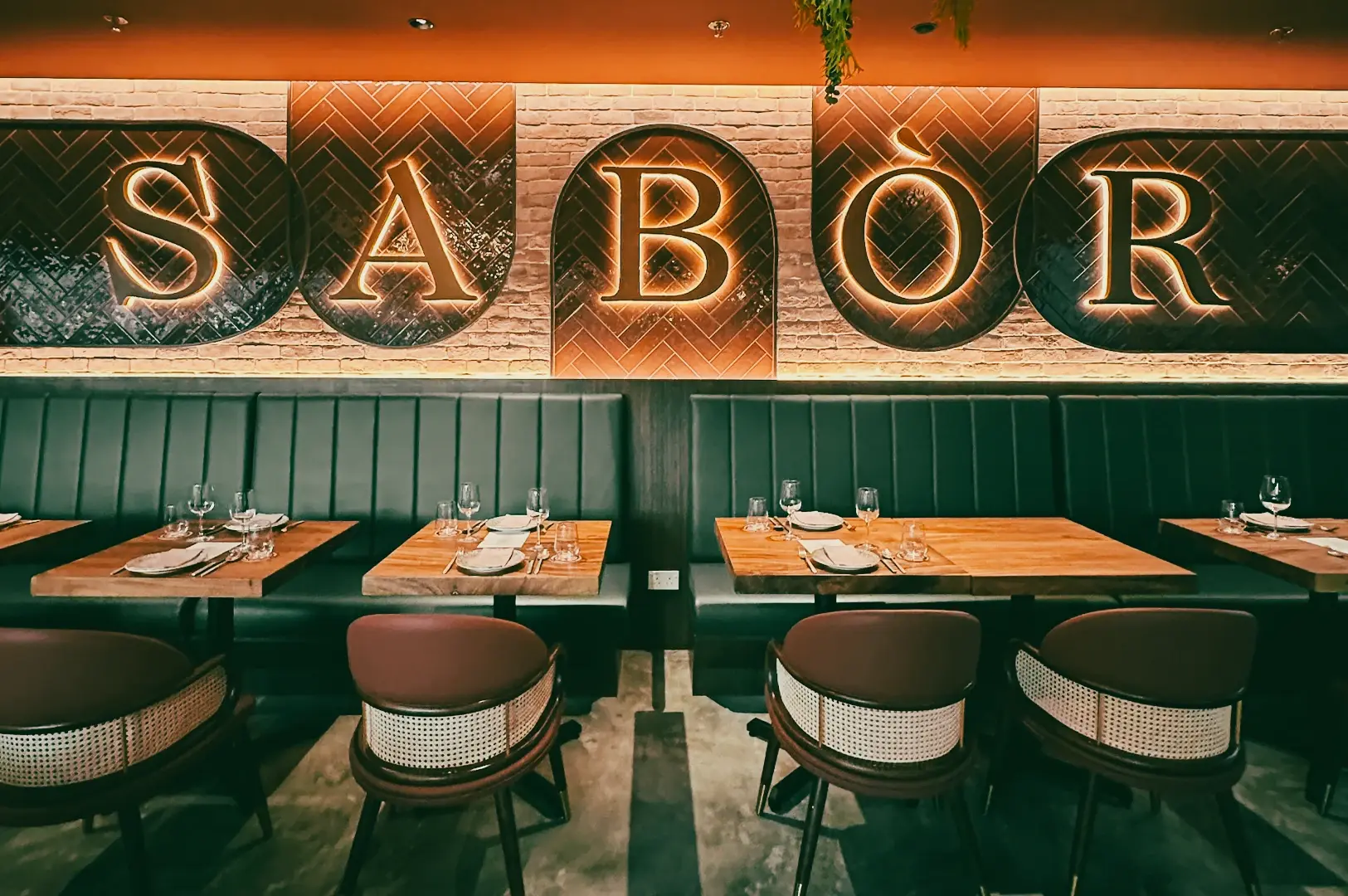 Wide-angle eye-level shot of Sabor restaurant interior at CHIJMES Singapore with illuminated “Sabor” wall signage, cozy booth seating, and modern Spanish tapas dining ambiance