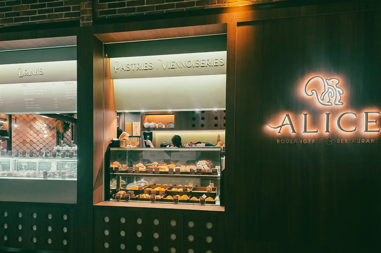 Eye-level exterior shot of Alice Boulangerie bakery cafe in Singapore showcasing pastries display and modern specialty coffee shop atmosphere at night