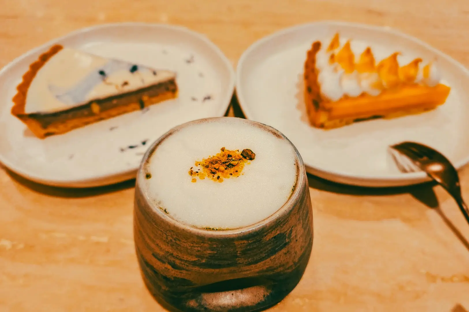 Close-up eye-level shot of specialty coffee with milk foam served alongside artisan desserts in a Singapore bakery cafe, highlighting cafe food pairings and local coffee culture