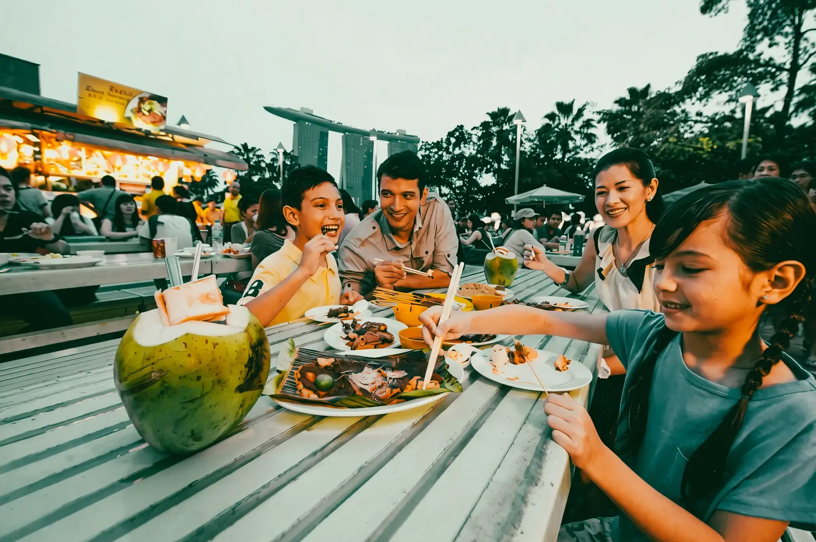 Outdoor dining in Singapore with family enjoying local food near Marina Bay Sands skyline, capturing vibrant dining scene and modern food culture Singapore, wide-angle lifestyle shot