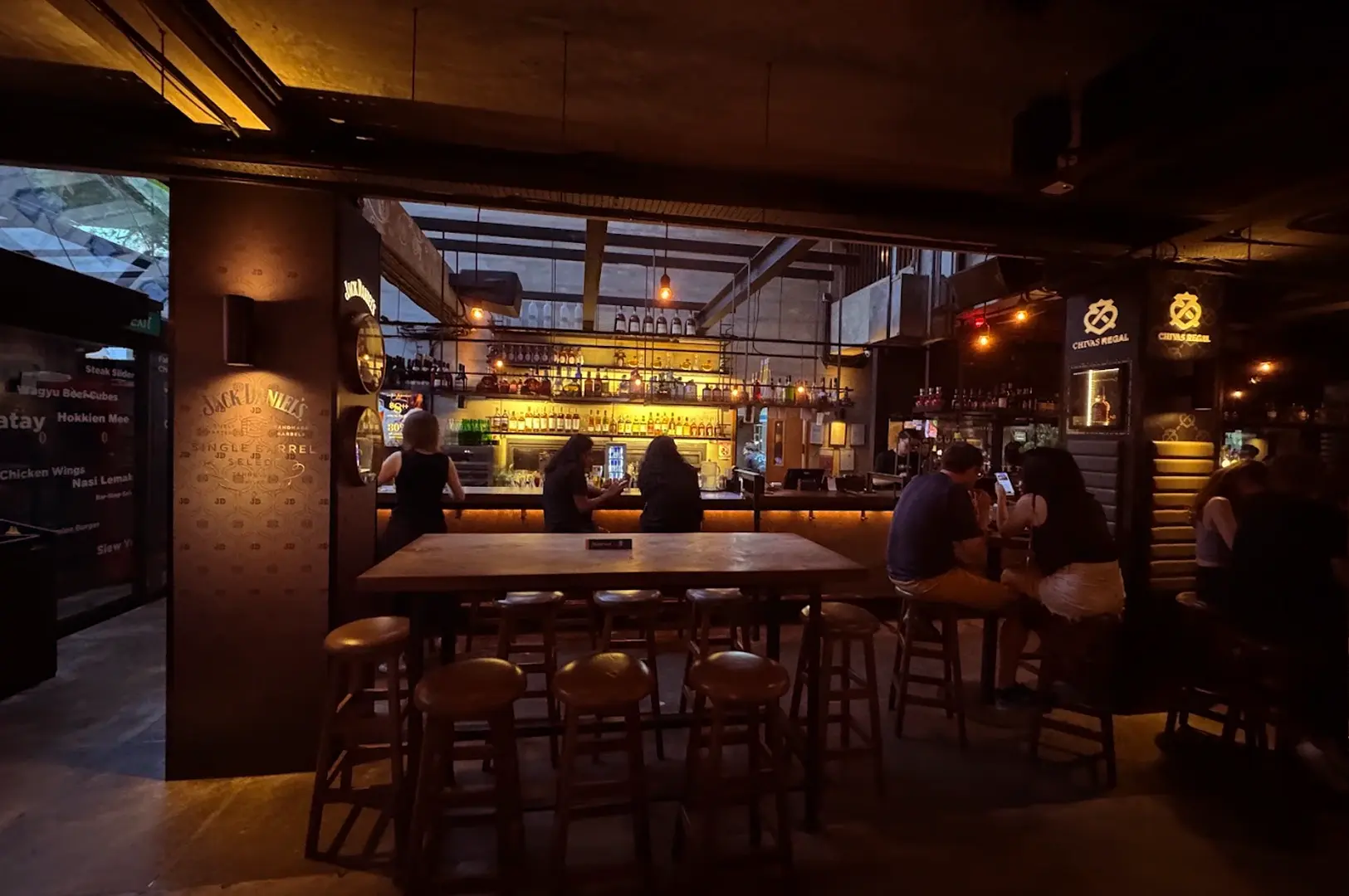The interior bar area of KPO Café Bar, featuring high-top seating, industrial-chic lighting, and a well-stocked bar counter perfect for nightlife.